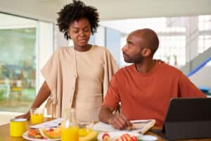 Black woman and man with newspaper and tablet at wooden table with orange juice and lunch meal chatting