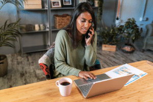 Hispanic self-employed woman during phone call and working on laptop from her home office