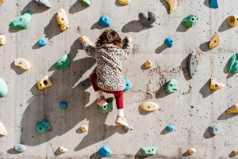 Little girl overcoming with an effort to climb a climbing wall