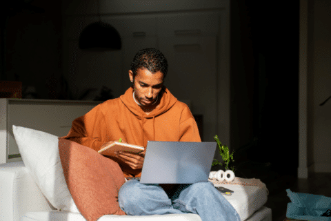 Man using laptop while sitting on couch at home. He is looking at the screen. he works from home and watches a movie online