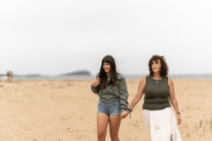 Mother and daughter holding hands and smiling while walking on the beach together in the daytime.