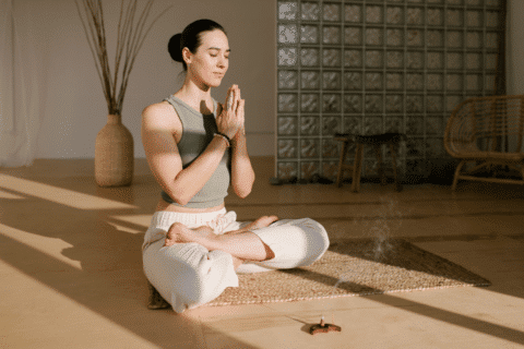 Woman sitting in Padmasana pose with closed eyes and meditating at sunny yoga studio